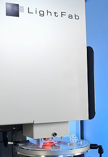 LightFab Hochgeschwindigkeits-Mikroscanner mit integriertem x-y-Tisch, schneller Fokussiereinheit und Mikroskop hinter der blauen Schiebetür